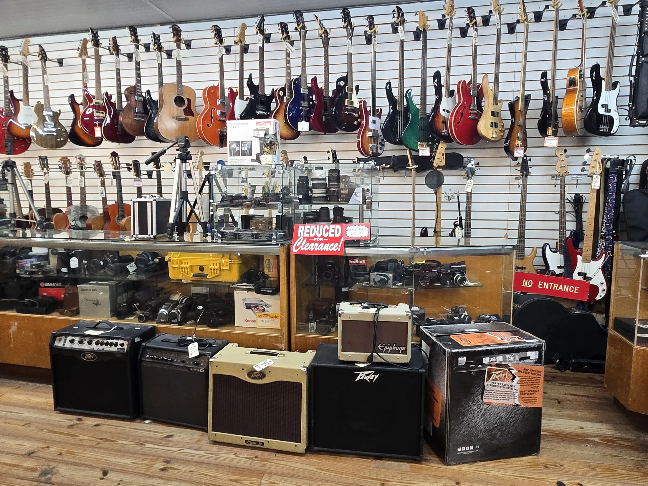 Guitars on the wall above amplifiers and cases at AAA Gun & Pawn